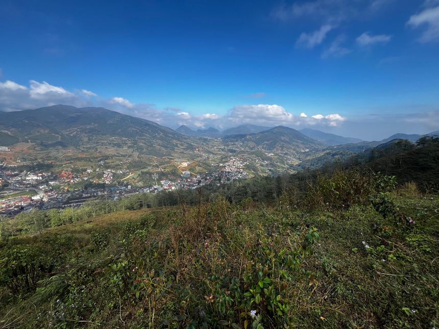 View from a grassy hillside over Sa Pa town and the mountains under a blue sky